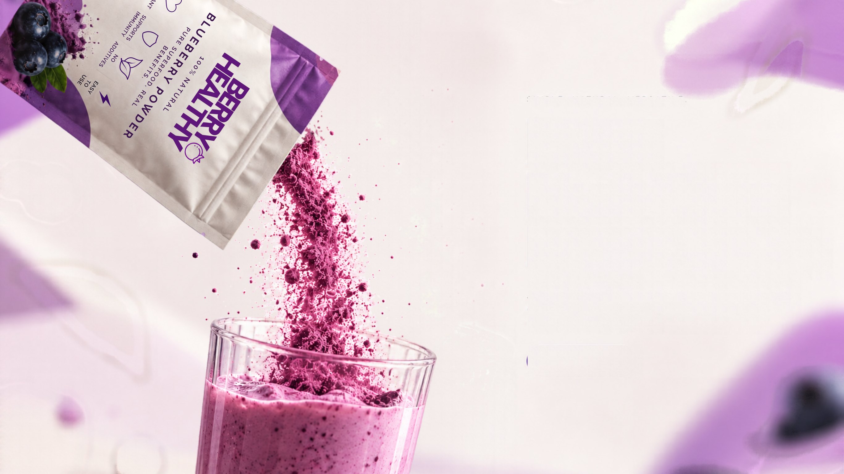 Berry Healthy blueberry powder pouch tilted to pour a stream of purple powder into a glass of purple blueberry smoothie, with soft-focus blueberries and leaves around it.